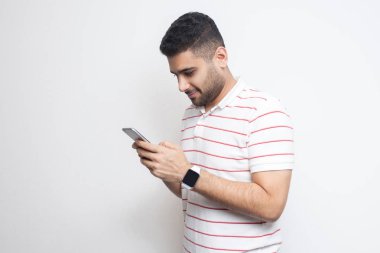 mutlu yakışıklı blogger genç yetişkin adam beyaz arka plan izole gülümseme ile akıllı telefon ve mesajlaşma mesajı kullanarak t-shirt giyiyor