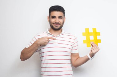 Kameraya bakarken elinde büyük büyük sarı hashtag işareti parmak ile işaret t-shirt Pozitif genç yetişkin adam , Yeni sosyal medya kavramı 