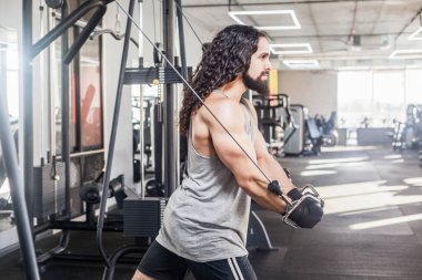 Halkalar üzerinde çalışırken ve spor salonunda trx egzersizleri yaparken uzun kıvırcık saç eğitim göğüs ile genç yetişkin kendinden emin adam Yan görünümü 