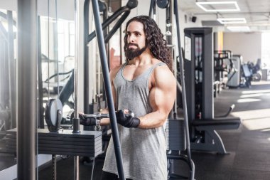 uzun kıvırcık saçlı genç yetişkin spor atlet adam ayakta ve spor salonunda ağırlık kaldırma sırasında pazı için egzersiz ler yapıyor 