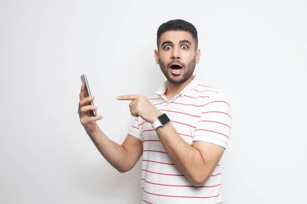Järkyttynyt Nuori Aikuinen Mies Valkoisessa Paidassa Osoittaa Sormella Älypuhelinta Kädessä — kuvapankkivalokuva