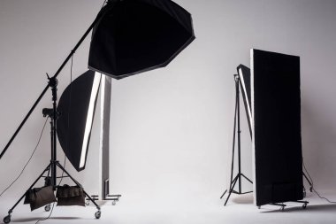 Professional photo studio with light setup and octagon softbox on boom with strip softbox and reflector on light gray background  clipart