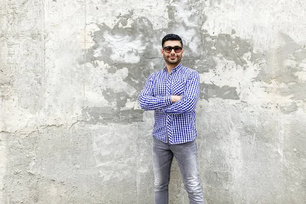 Beton arka plan üzerinde duran damalı mavi gömlek güneş gözlüğü ile başarılı sakallı genç adam Portresi 