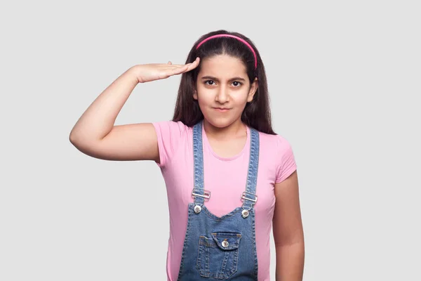 Serious Brunette Young Girl Pink Shirt Blue Overalls Showing Salute — Stock Photo, Image