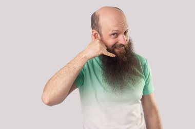 arama el hareketi gösteren ve gri arka planda kamera bakarak açık yeşil t-shirt uzun sakallı mutlu orta yaşlı kel adam