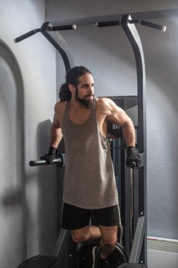 elleri ile yatay barda asılı uzun kıvırcık saçlı genç yetişkin güçlü adam ve spor salonunda pull up yapıyor, triceps için egzersizler 