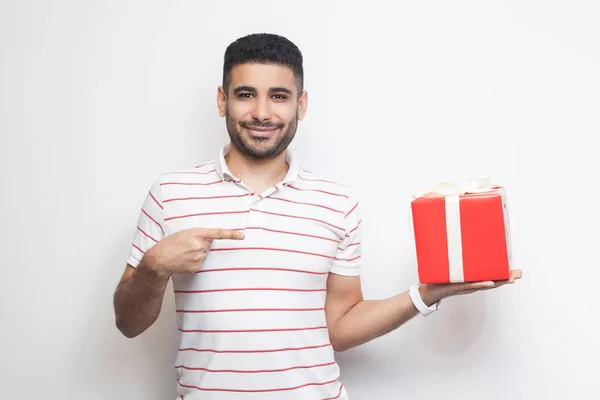 Alegre Joven Adulto Hombre Camiseta Sosteniendo Caja Regalo Roja Señalando —  Fotos de Stock