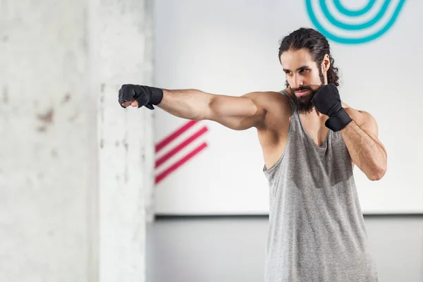 愤怒的肌肉年轻男子与黑手套卷曲的头发显示专业拳击技术在健身房 — 图库照片