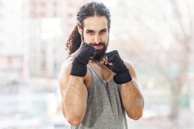 pencereyakınında ağır kolları ile ayakta iken poz mücadele yumruktutan ve kameraya bakarak kıvırcık uzun saçlı kendine güvenen sportif genç yetişkin kas eğitmen adam 