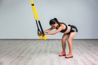 Spor kıyafetli genç, formalı bir kadın spor salonunda spor kemerleriyle çömelme egzersizi yapıyor. Trx işlevsel eğitim kavramı    