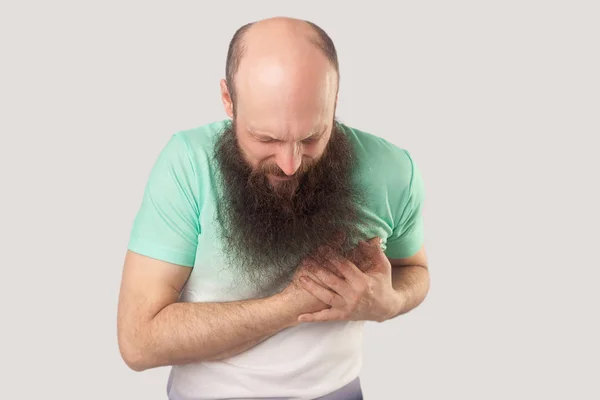 病気の中年ハゲひげの男は 彼の胸を保持し 灰色の背景に心の痛みを感じる緑のTシャツを着て — ストック写真