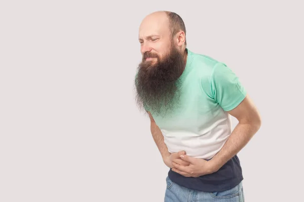 生病的中年秃头男子长胡子浅绿色T恤抱着他痛苦的肚子和感觉不好的灰色背景 — 图库照片