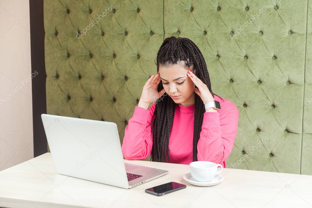 thoughtful sad young woman freelancer with black dreadlocks hairstyle holding head down and thinking while sitting at table with laptop in cafe , freelancing concept 