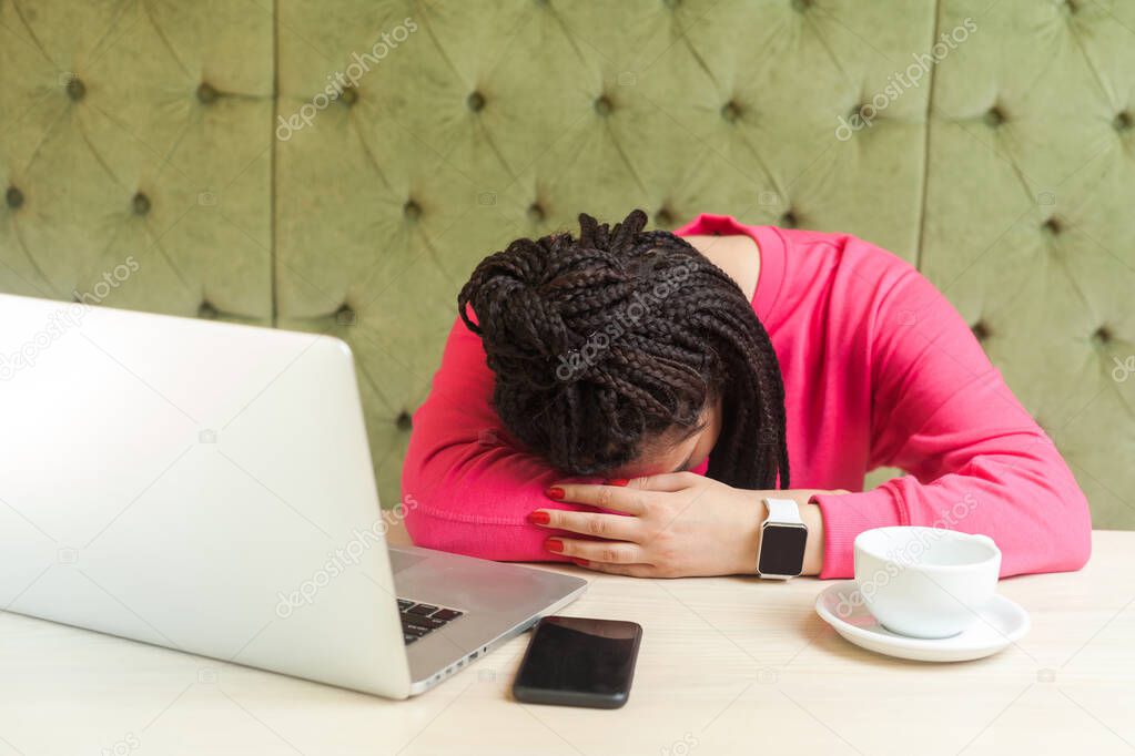 tired kind beautiful young freelancer with black dreadlocks in pink blouse sleeping while sitting at table with laptop in cafe 