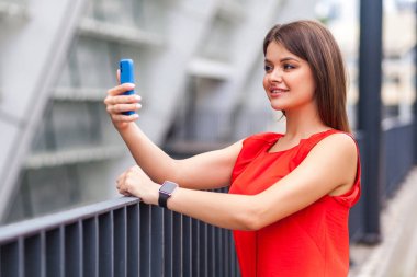 Half turned portrait of beauty blogger woman in red t-shirt looking selfish and confident while taking selfie on smartphone 