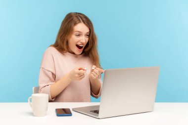 Vay canına, inanılmaz! Şaşırmış, heyecanlı kadın çalışan dizüstü bilgisayarı işaret ediyor, şok edici haberler okuyor ya da video karşısında hayret verici bir ifadeyle konuşuyor. Mavi arka planda kapalı stüdyo çekimleri