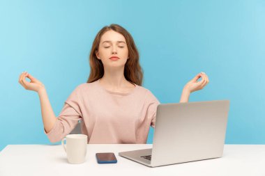 Peaceful mind, break at work. Calm woman employee sitting at workplace with laptop and raising hands in mudra gesture, meditating resting at home office. indoor studio shot isolated on blue background clipart