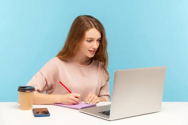 女性ジャーナリストはノートパソコンで作業し 紙にメモを作る オンライン学校 インターネットコースを聞きながらノートに書き込み 学生の勉強 青い背景に隔離された屋内スタジオで — ストック写真