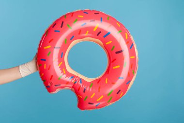 Pembe Lifebuoy tutan beyaz cerrahi eldivenli insan elinin profil yan görüntüsü. Yaz ve tatil konsepti. İçerde, stüdyoda, mavi arka planda izole edilmiş..