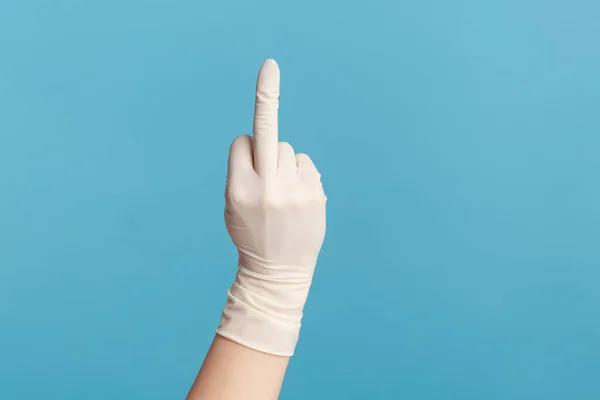 Profile side view closeup of human hand in white surgical gloves showing middle finger. indoor, studio shot, isolated on blue background.