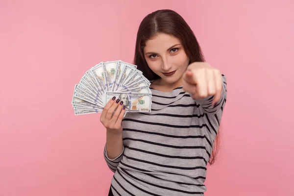 お金を稼ぐ 縞模様のスウェットシャツの若い女性の肖像カメラを指してドル紙幣を保持し 宝くじに勝つために奨励し 利益を得る ピンクの背景に隔離されたスタジオショット — ストック写真
