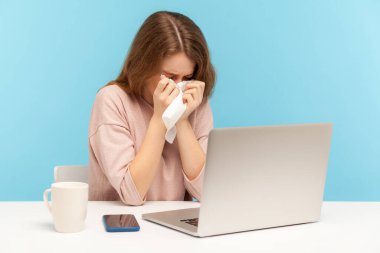 Depresyondaki aşırı çalışan kadın çalışanlar ağlıyor ve gözyaşlarını mendille siliyor, iş sıkıntıları konusunda endişeli ve umutsuz hissediyor, iş yerinde ev ofisinde oturuyor. İç mekan stüdyo çekimi, mavi arka plan