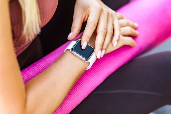 Closeup female holding pink yoga mat and checking pulse on smartwatch after sport trainings, looking at wristwatch black empty display, technology device with calories count app, weight loss program