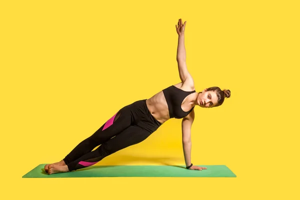 侧板的姿势 身强体壮的女孩穿着紧身运动服练习瑜伽 单手举手表决练习 锻炼肌肉 演播室拍摄 每日运动训练隔离在黄色背景下 — 图库照片