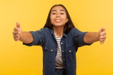 Kollarıma gel! Dost canlısı cömert kız portresi. Kucaklaşmak için ellerini açık tutuyor, sıcak bir karşılama yapıyor, mutlu bir gülümsemeyle selamlıyor. Stüdyo çekimi sarı arkaplanda izole edildi
