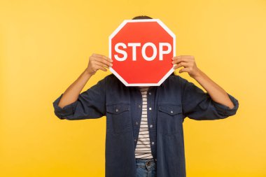 Dikkat, yasak yol! Kot gömlekli bilinmeyen kişi dur sembolünün arkasına saklanıyor, kırmızı trafik işareti yasak giriş uyarısı, yasaklanmış servis uyarısı. Sarı arka planda izole edilmiş kapalı stüdyo çekimi