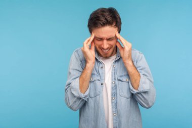 Kotlu gömlekli sağlıksız bir adamın portresi parmaklarını şakaklara bastırıyor, hasta ve şiddetli baş ağrısı çekiyor, stres migreni, gerilim. Mavi arka planda kapalı stüdyo çekimleri