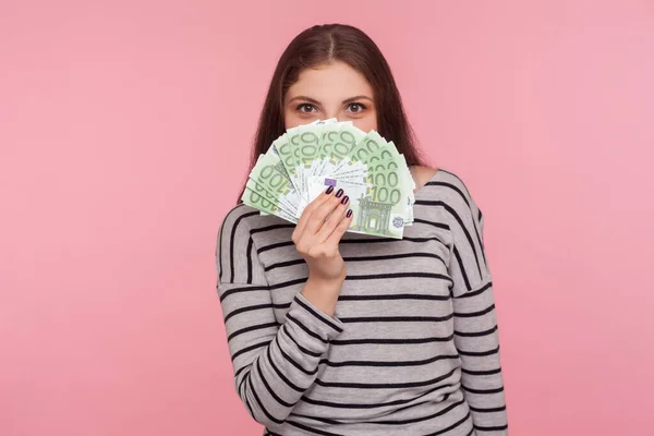 宝くじの勝者の肖像画 縞模様のスウェットシャツの若い幸せな女性は 遊び心のある外観でユーロ紙幣をのぞき見 大きなジャックポット 財政的な成功を楽しんでいます ピンクの背景に隔離されたスタジオショット — ストック写真