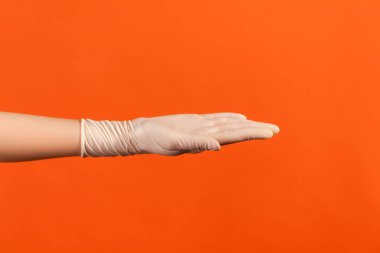 Profile side view closeup of human hand in white surgical gloves showing hand. indoor, studio shot, isolated on orange background.