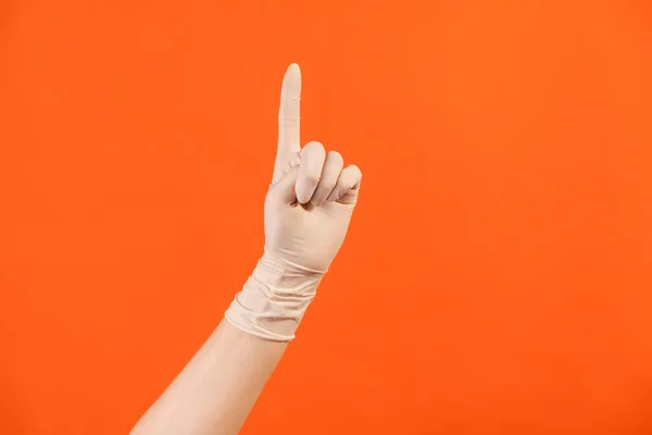 Profile side view closeup of human hand in white surgical gloves showing number one with finger or showing up side. indoor, studio shot, isolated on orange background.