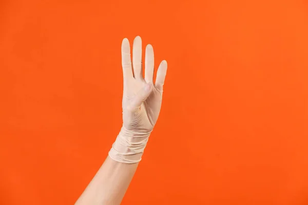 Profile side view closeup of human hand in white surgical gloves showing number four 4 with hand. indoor, studio shot, isolated on orange background.