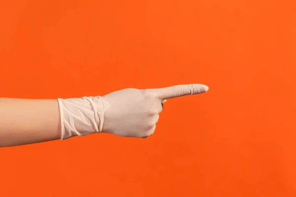 Profile side view closeup of human hand in white surgical gloves showing or pointing ot something with finger. indoor, studio shot, isolated on orange background.