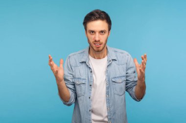 Aggression and conflict. Portrait of irritated man in worker denim shirt raising hands and clenching teeth with anger, hate emotions, annoyed by problem. indoor studio shot isolated on blue background