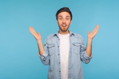 Oh my god, wow! Portrait of astonished man in worker denim shirt raising hands in amazement, looking with open mouth, big eyes, feeling shocked and happy about unexpected success. studio shot isolated