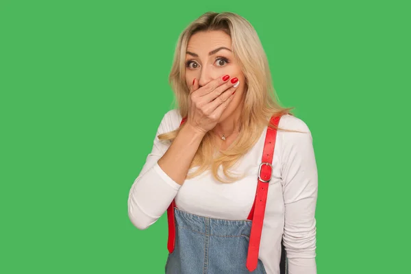 I won\'t speak! Portrait of frightened intimidated adult woman covering mouth with hand and looking scared, afraid to tell truth, keeping terrifying secret. studio shot isolated on green background