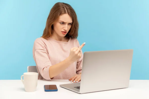 中指ノートパソコンの画面を見せる無礼な若い女社員たちは ビデオ通話で積極的にコミュニケーションを取り 不敬と憎悪を表明 青い背景に隔離された屋内スタジオで — ストック写真