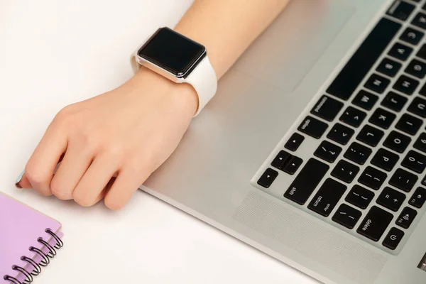 Top view, closeup of woman journalist, businessperson with smart wristwatch sitting at workplace, laptop, phone, paper notebook with glasses on desk. indoor studio shot isolated on blue background