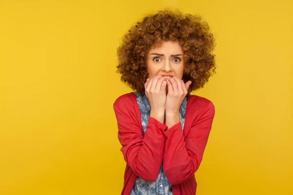 Depression, anxiety disorder. Portrait of stressed out, worried woman with curly hair biting nails and looking terrified, nervous about troubles. indoor studio shot isolated on yellow background