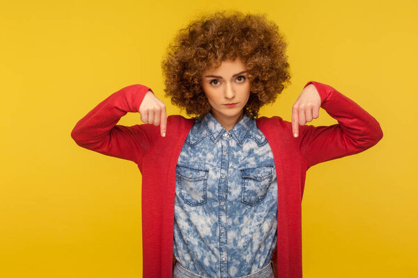 Вы должны начать прямо сейчас! Портрет рассерженной властной женщины с вьющимися волосами, указывающей пальцем вниз, отдающей приказы с требовательным выражением, концепцией контроля. Крытая студия снята на жёлтом фоне
