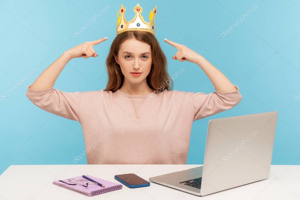 Look, I am boss here! Proud ambitious egoistic narcissistic businesswoman pointing at crown on head and looking with arrogance, over-inflated ego. indoor studio shot isolated on blue background