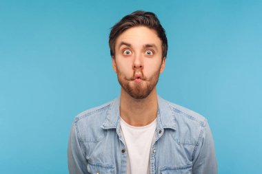 Komik balık suratlı, dudak bükmüş dudaklı ve şaşkın, aptal aptal ifadesiyle yüzünü ekşiten işçi kot gömlekli komik adamın portresi. Mavi arka planda kapalı stüdyo çekimleri