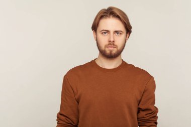 Kendine güvenen, sakallı, düzgün saçlı, kazak giyen ve kameraya dikkatlice bakan yakışıklı bir adamın portresi. Gri arka planda kapalı stüdyo çekimi