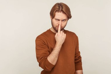 Yalan söyleme bana! Tişörtlü kızgın sakallı bir adamın portresi parmağıyla burnuna dokunuyor, yalancı jest gösteriyor, aldatmadan şüpheleniyor, iletişimde yalan söylüyor. Stüdyo çekimi gri arkaplanda izole edildi