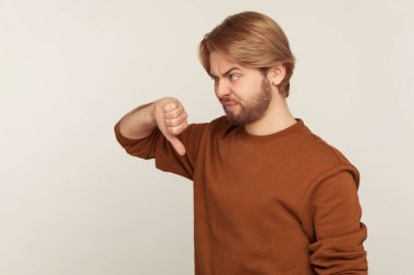 Bundan hoşlanmadım! Sweatshirt 'lü hoşnutsuz sakallı bir adamın portresi. Başparmaklarını göstermiyor ve hayal kırıklığına uğramış görünüyor. Öneriye katılmıyor. Gri arka planda kapalı stüdyo çekimi