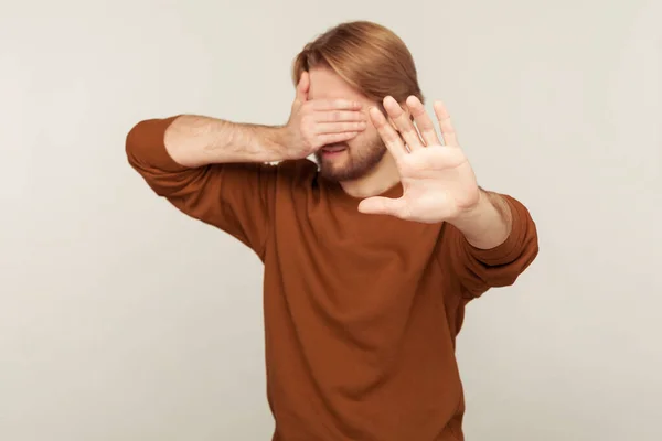 No, don\'t want to look! Portrait of confused man covering eyes and raising hand to stop, feeling stressed afraid, refusing to watch scary content, avoiding troubles. indoor studio shot isolated