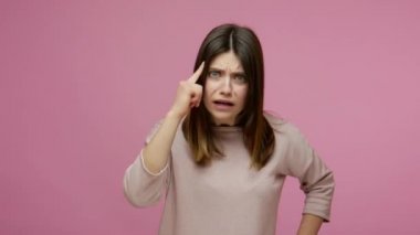 Are you insane? Displeased brunette woman showing stupid gesture and pointing to camera, expressing disagreement with senseless dumb suggestion, bad mind, crazy plan. indoor studio shot, isolated